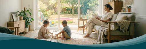 Living room with large windows facing the garden. Children play on a rug while a person reads on the sofa. Zehnder residential ventilation ensures air exchange.