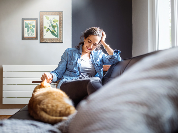 Beautiful young woman relaxing on sofa with her cat in living room.