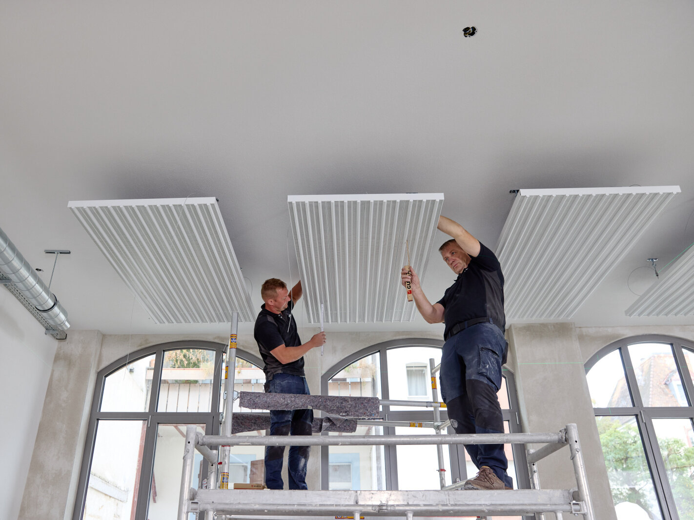 Zwei Handwerker montieren eine Deckenstrahlplatte von Zehnder wie sie es im Web-Seminar gelernt haben